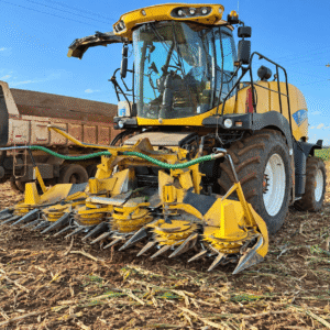 Colhedora de forragem New Holland vista de frente, com plataforma de milho amarela e caminhão ao lado.