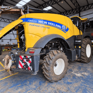 Colhedora de forragem New Holland FR500 vista pela lateral e traseira, com tampa de acesso aberta dentro de um galpão.